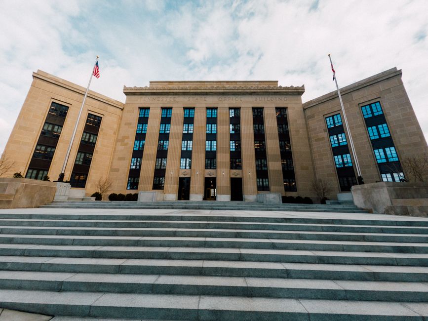 From below of Federal Reserve building exterior against USA flags and staircase under cloudy sky in town